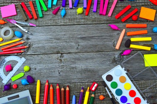 bunte Stifte, Kreide, ein Farbkasten und ein Linial liegen auf einem Tisch in einem Kreis.