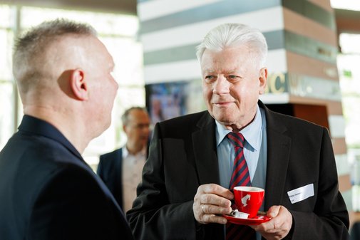 Peter Jeromin, Vize-Pr&auml;sident des VdK NRW, unterh&auml;lt sich mit einem Gast und h&auml;lt dabei eine rote Tasse Kaffee in der Hand.