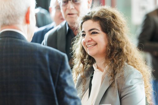 eine Dame mit langen Locken tr&auml;gt ein Sakko und l&auml;chelt einen Mann freundlich an.