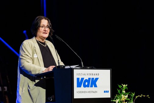 Katharina Batz, Vize-Pr&auml;sidentin des VdK, steht an einem Pult mit der Aufschrift VdK. Sie hat schwarze Haare, tr&auml;gt eine Brille und ein beiges Sakko.