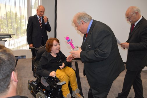 Eine vilmA-Preisträgerin im Rollstuhl bekommt den Preis vom Laudator überreicht.
