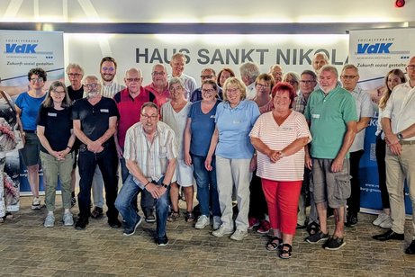 Eine gro&szlig;e Gruppe Frauen und M&auml;nner steht gemeinsam vor einer Wand mit Aufschrift Haus Sankt Nikolaus. Rechts und links von ihnen Roll-Ups mit VdK-Logo.