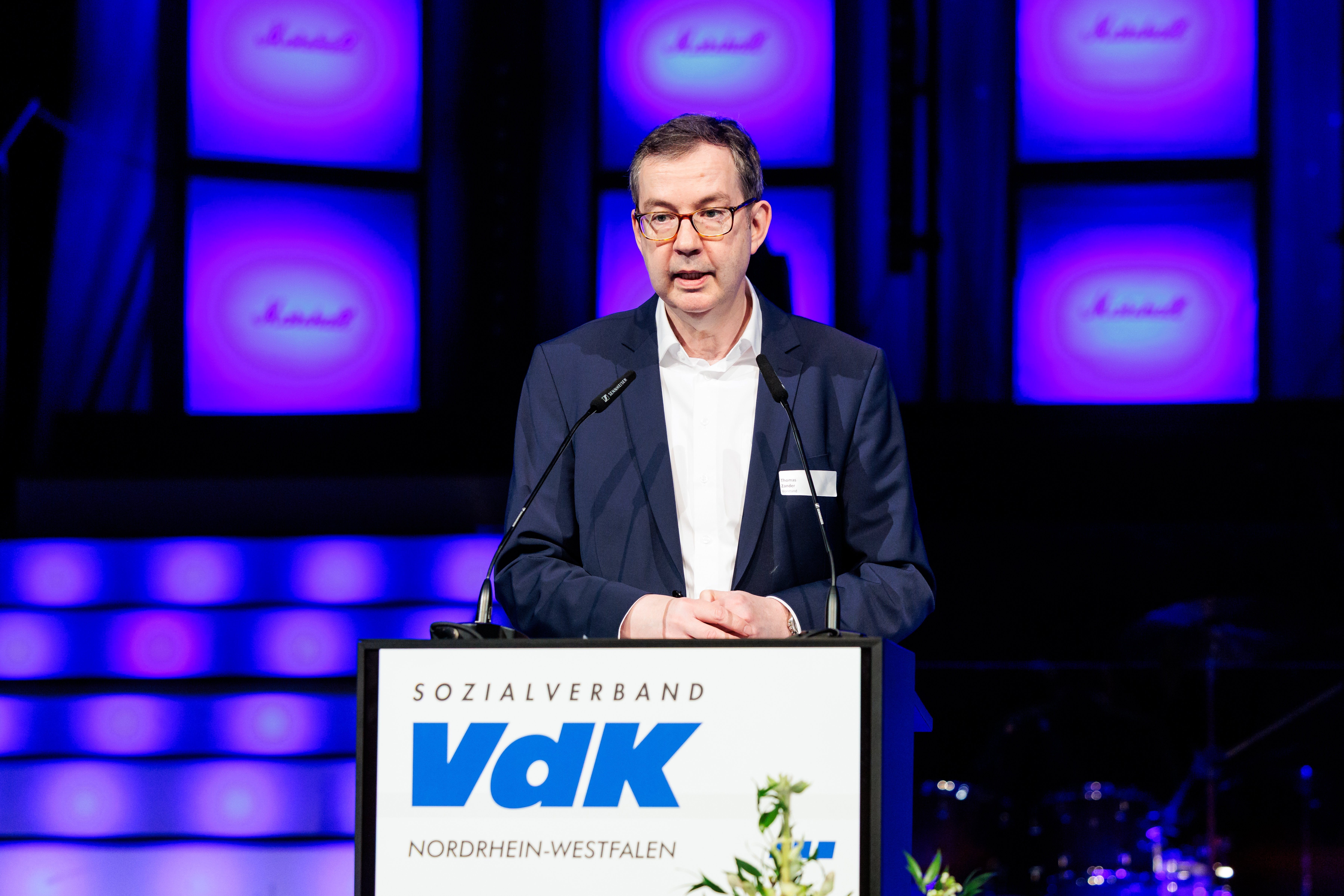 Ein Mann im Anzug mit Brille und Kurzhaarfrisur steht an einem Rednerpult mit VdK-Logo und spricht in ein Mikrofon.