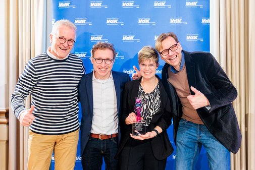 Gruppenbild einer Preisträgerin und ihrer drei Begleiter vor der VdK-Pressewand. 