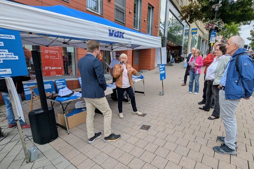 interessierte Bürgerinnen und Bürger hören einem Interview zwischen Benedikt Lechtenberg und Susanne Otto vor dem VdK-Stand zu.