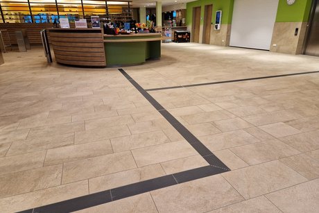 Ein taktiles Leitsystem auf dem Boden f&uuml;hrt zum Holztresen der Schwimmbadkasse und weiter zu den Umkleideberreichen.