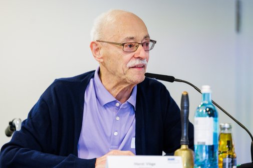 VdK-Pr&auml;sident Horst V&ouml;ge spricht in ein Mikrofon. Er tr&auml;gt eine blaue Jacke und ein lila Hemd sowie eine Brille