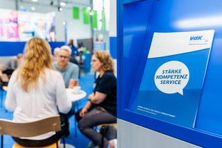 Broschüre mit VdK-Leitbild im Vordergrund. Im Hintergrund Besucher an einem Tisch am Stand.