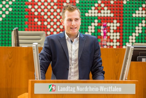 Ein junger Mann in Sakko an einem Rednerpult.