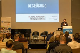 Dr. Klaus Kordowski, Projektmanager bei der Stiftung Mercator, steht am Rednerpult auf der Bühne und begrüßt die Gäste.