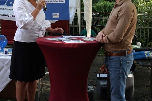 Eine Frau mit Mikrofon steht gemeinsam mit einem Mann an einem Stehtisch und spricht.