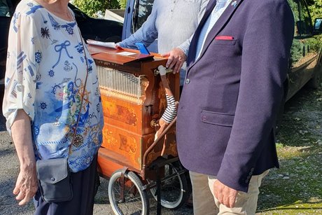 Eine Frau und ein Mann unterhalten sich, im Hintergrund spielt ein Mann eine Drehleier.