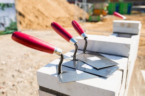 Zementschaufeln liegen auf Steinen, hinten ist liegt ein Berg voll Sand
