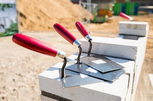 Zementschaufeln liegen auf Steinen, hinten ist liegt ein Berg voll Sand