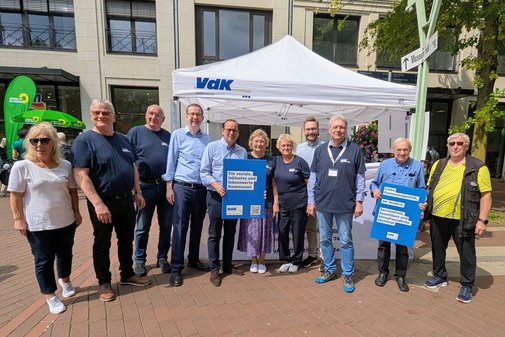 3 Frauen und 7 Männer haben sich in einer Reihe aufgestellt und lächeln in die Kamera. Zwei Männer halten Schilder hoch mit sozialpolitischen Forderungen des VdK.