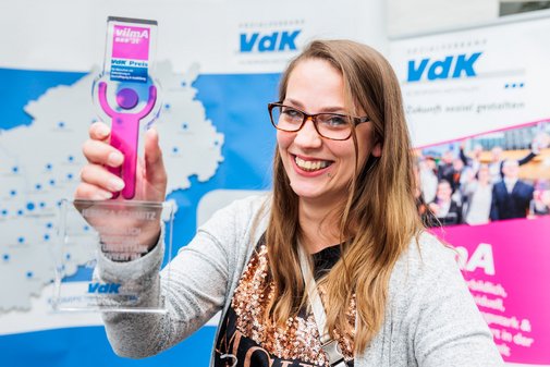 Eine vilmA-Preisträgerin hält lächelnd den Pokal in die Höhe