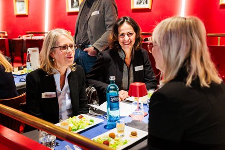 Drei Frauen sitzen im Gespräch an einem mit Vorspeisen gedeckten Tisch.