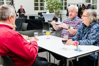 Mehrere Gäste sitzen bei Getränken ins Gespräch vertieft an einem Tisch.