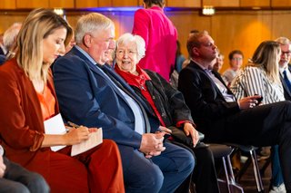 Menschen sitzen im bestuhlten Saal der Stadthalle Neuss nebeneinaner.