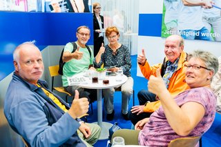 Eine Gruppe Menschen sitzt am Stand und reckt die Daumen in die Luft