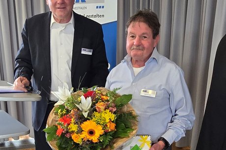 Peter Jeromin steht neben Manfred Daub, der einen großen Blumenstrauß hält.