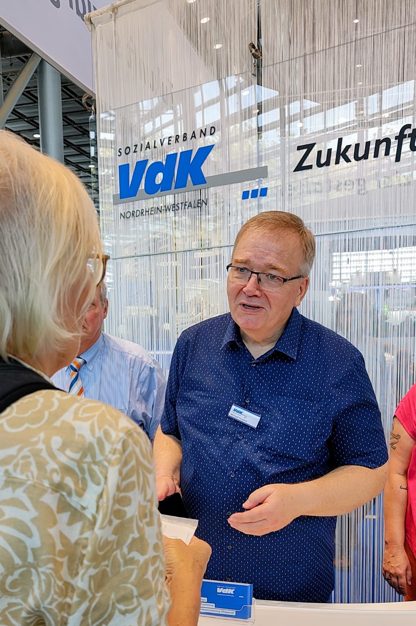 Michael Hummel (OV Meerbsuch) im Gespräch mit einer Messebesucherin am Tresen des VdK-Stands.