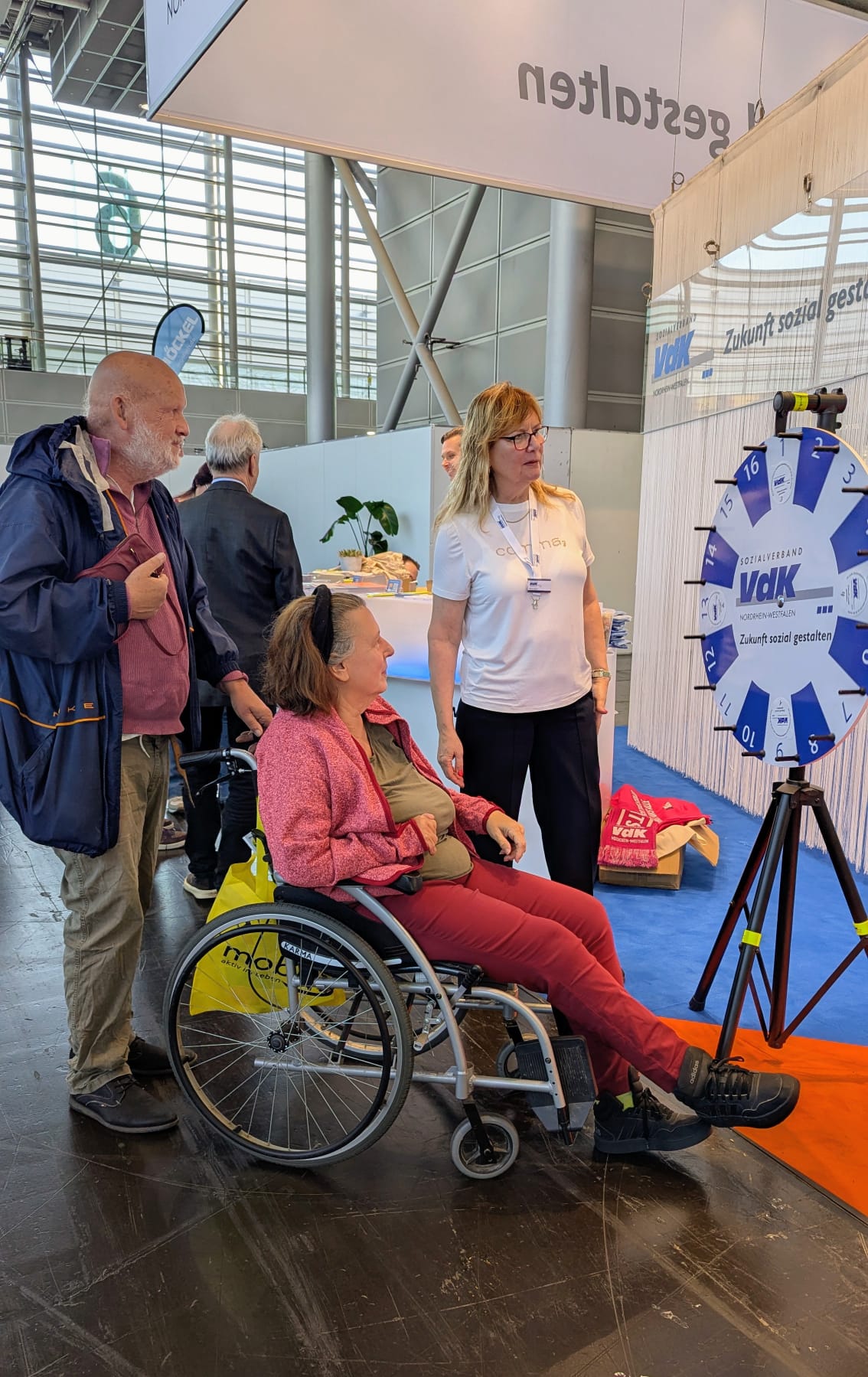VdK-Mitarbeiterin Silvia Born am VdK-Glücksrad mit Stand-Besuchern