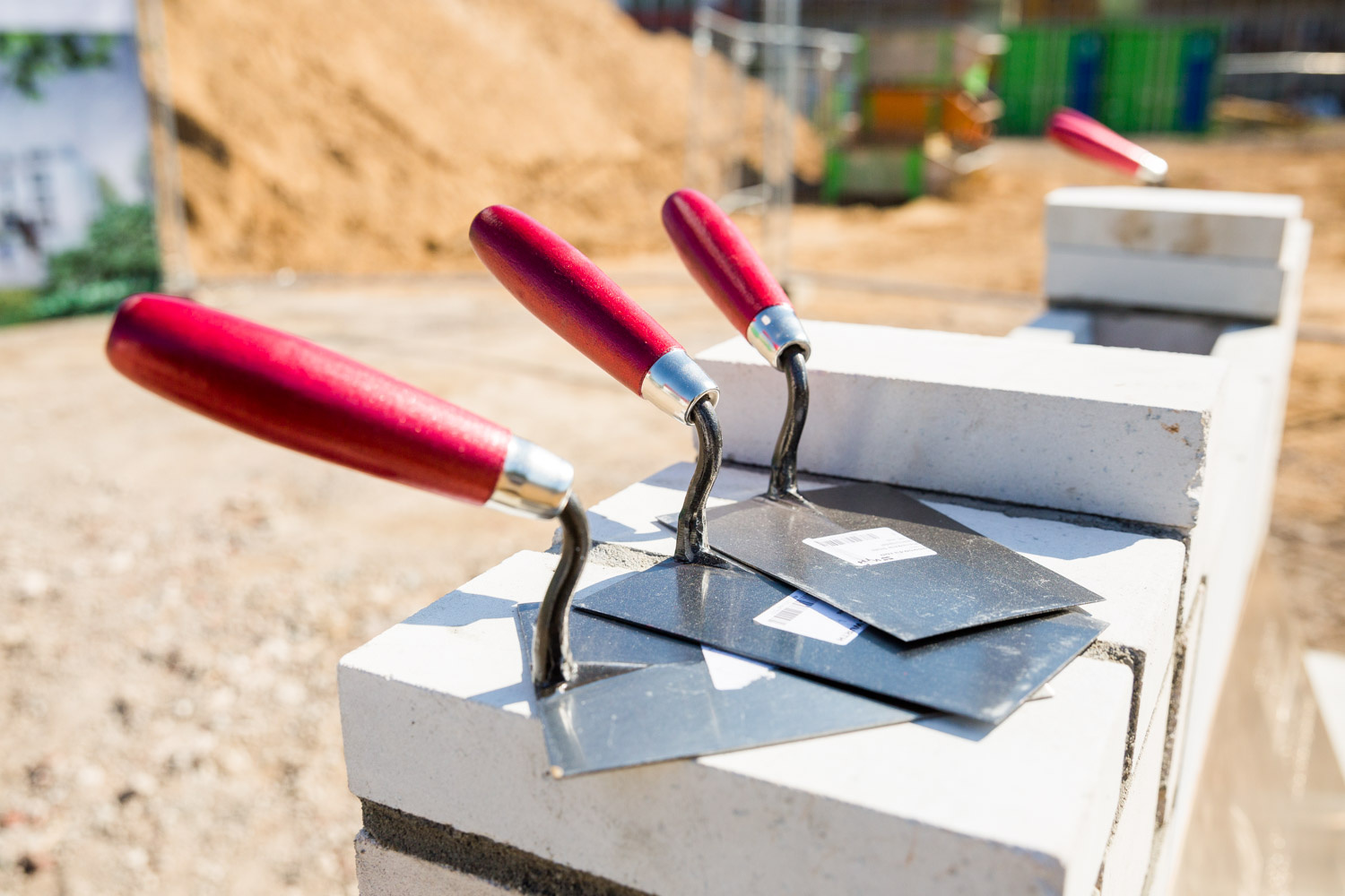 Zementschaufeln liegen auf Steinen, hinten ist liegt ein Berg voll Sand