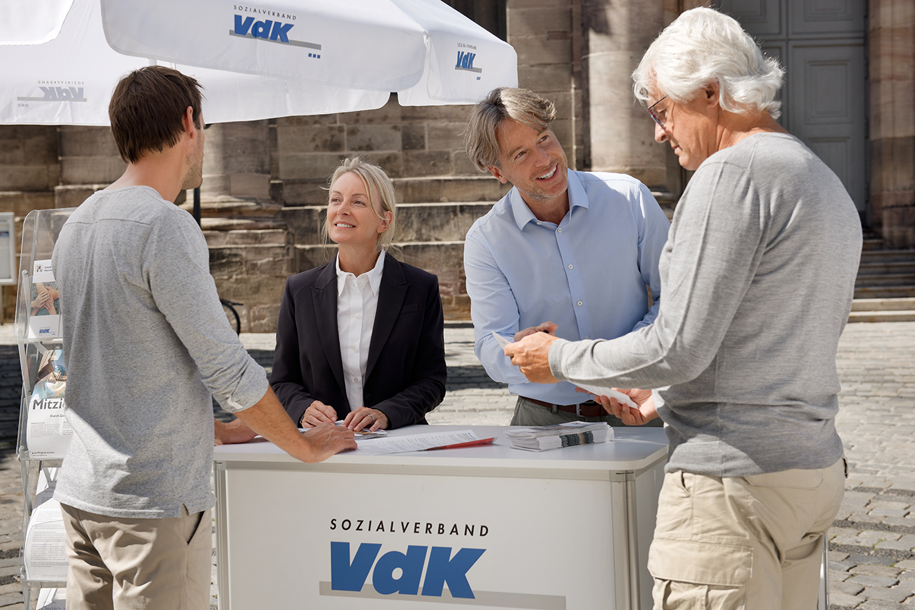 Menschen am VdK-Infostand Eine Mitarbeiterin und ein Mitarbeiter an einem VdK-Infostand informieren gerade zwei interessierte Passanten.