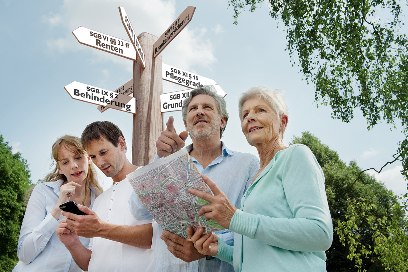 Ein j&uuml;ngeres und ein &auml;lteres P&auml;rchen suchen mit einer Karte nach etwas, hinter ihnen ein Wegweiser, auf dem verschiedene Begriffe aus dem Sozialrecht stehen. 