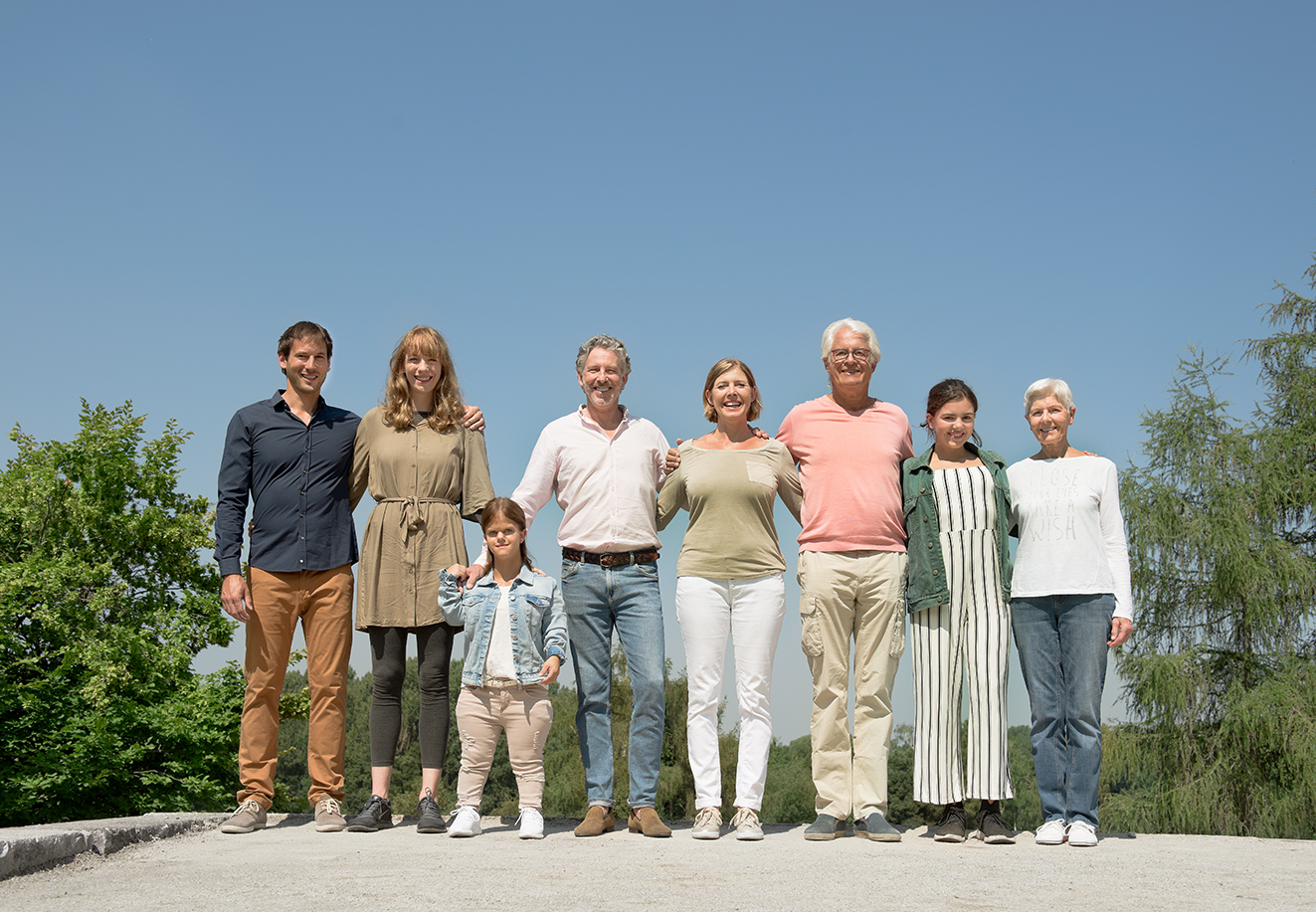 Menschen verschiedenen Alters mit und ohne Behinderung blicken lächelnd in die Kamera Menschen verschiedenen Alters mit und ohne Behinderung stehen untergehakt und lächelnd in einer Reihe in der Sonne