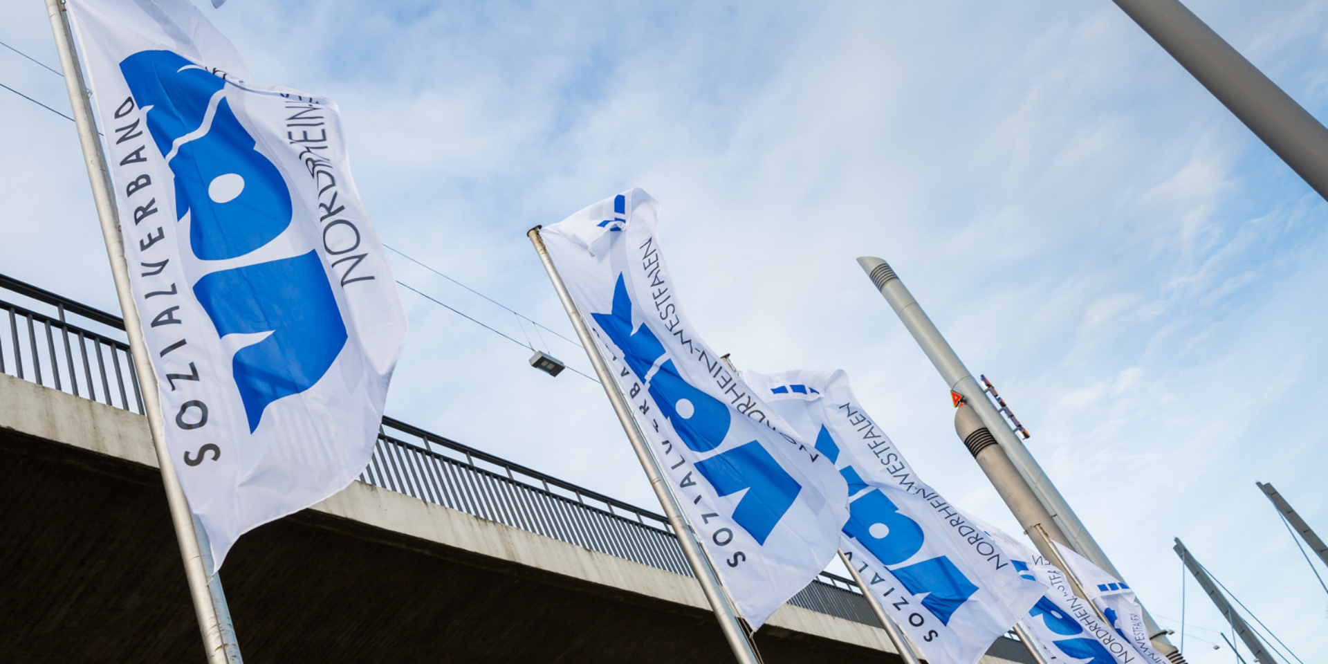 Fahnen mit VdK-Logo flattern vor blauweißem Himmel im Wind.
