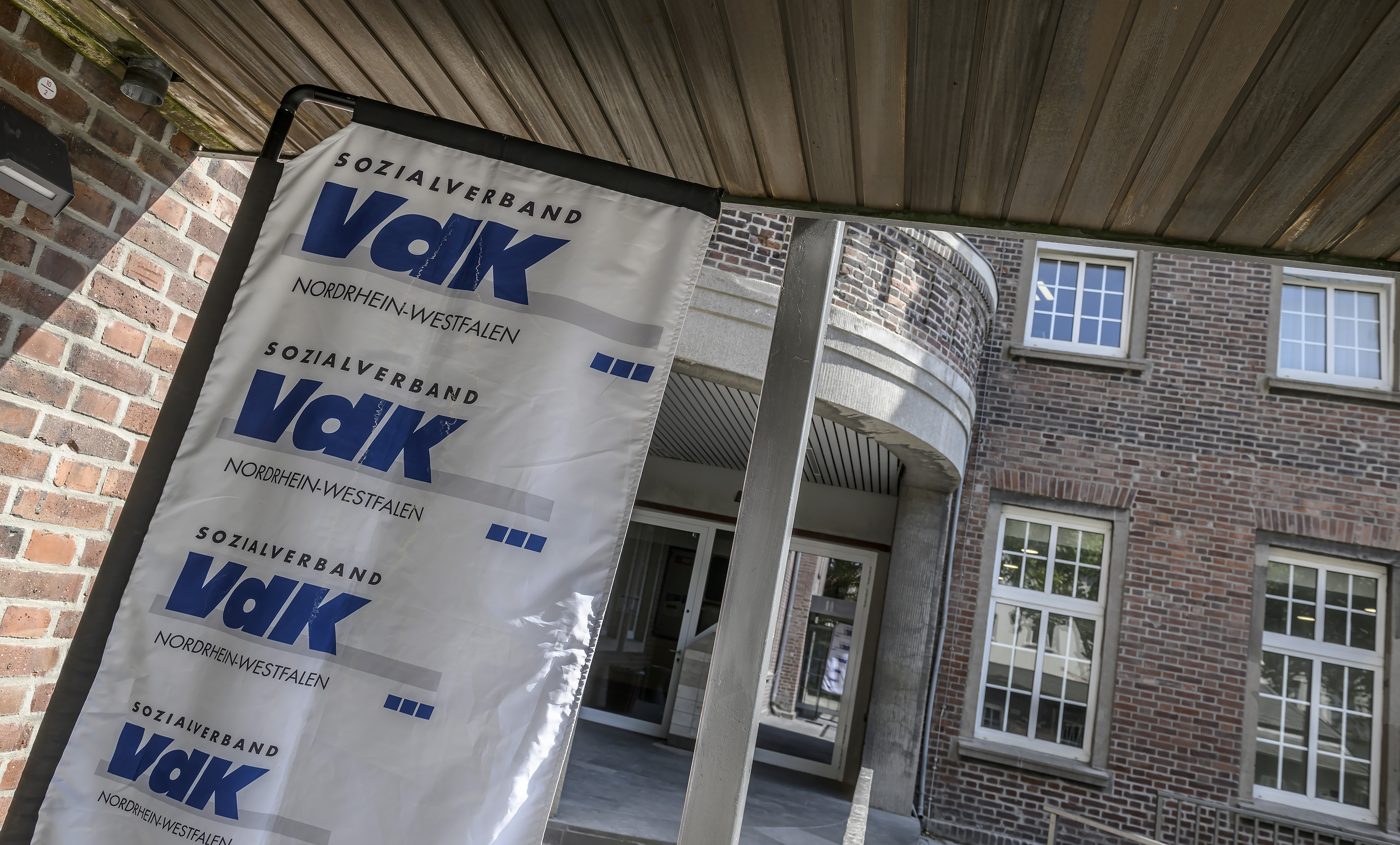 Eingangsbereich eines rotverklinkerten Geb&auml;udes mit VdK-Banner links daneben. 