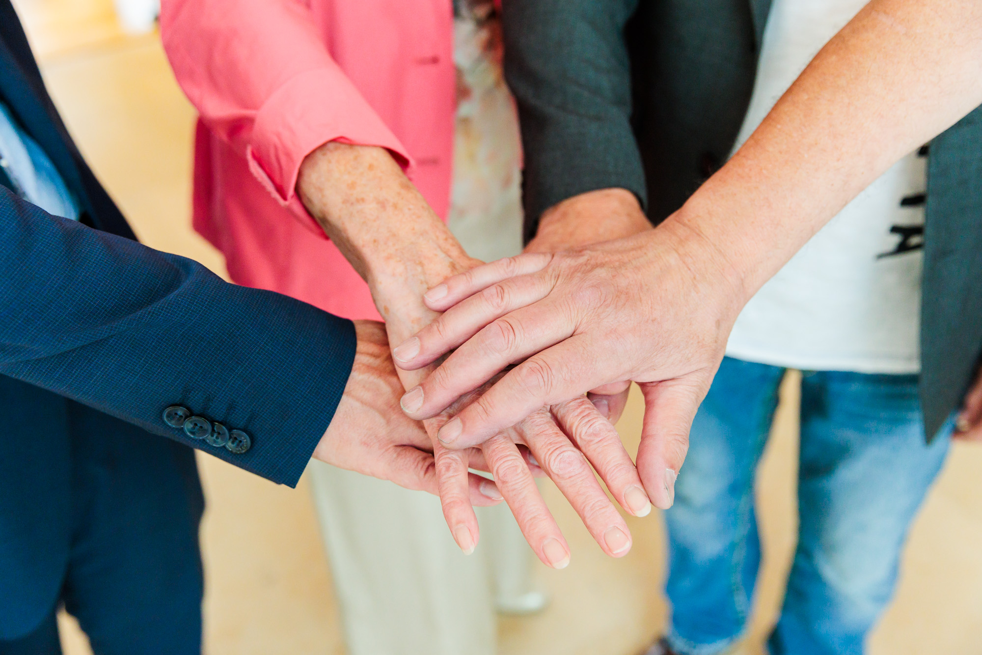 Vier Arme reichen ins Bild, die H&auml;nde in der Bildmitte &uuml;bereinandergelegt.