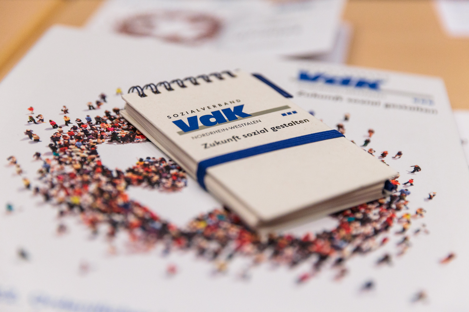 Ein Notizblöckchen mit blauem VdK-Logo liegt auf einer buntgemusterten Broschüre.