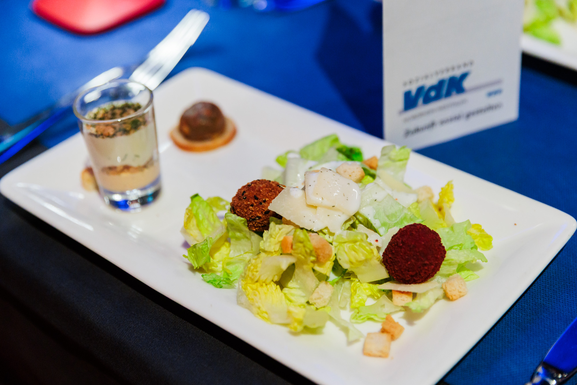Wei&szlig;er Teller mit Salat und kleinen H&auml;ppchen auf blauem Tischtuch.