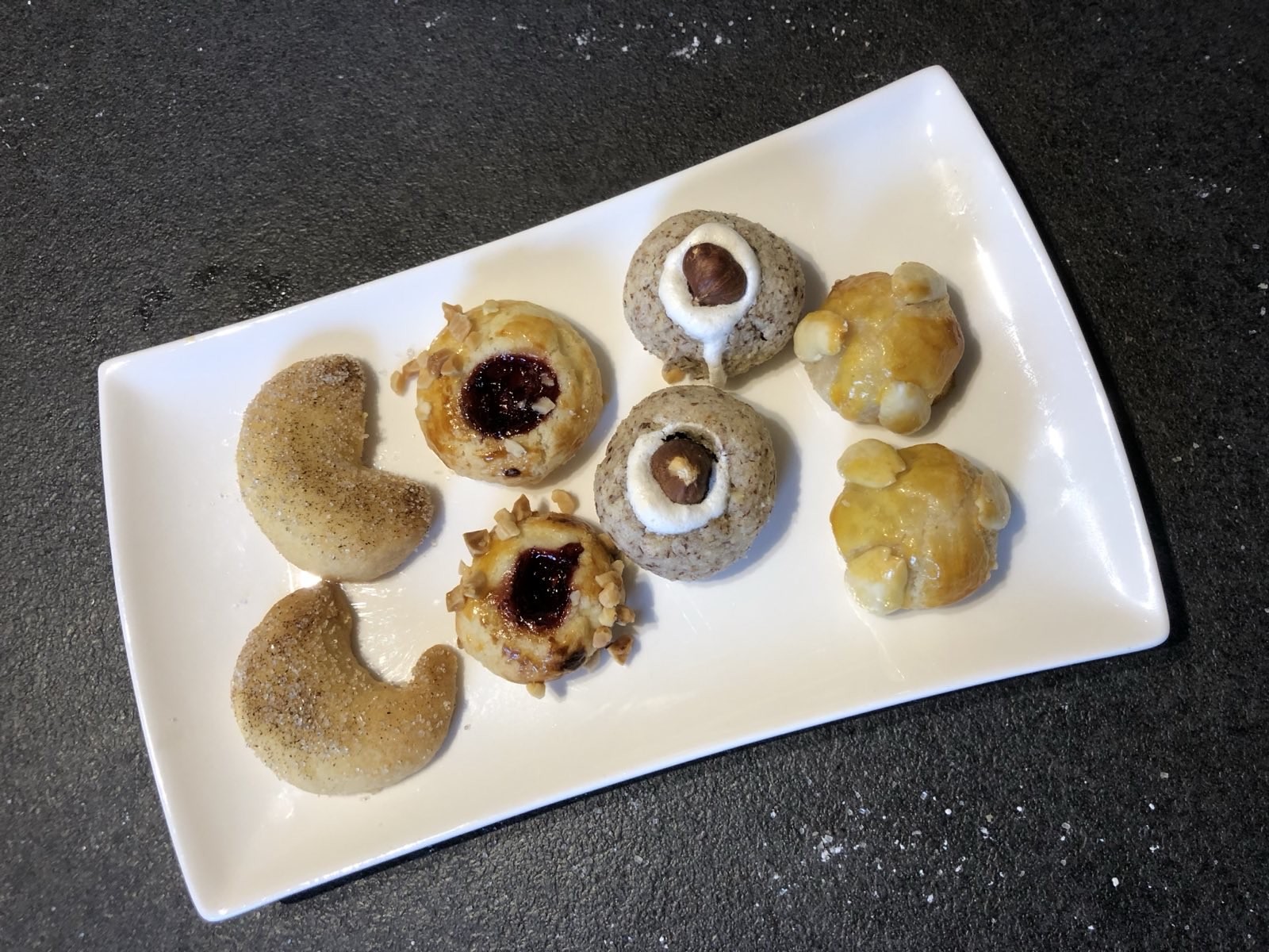 Vier verschiedene Sorten Weihnachtsplätzchen sind jeweils paarweise auf einem eckigen Teller angerichtet.