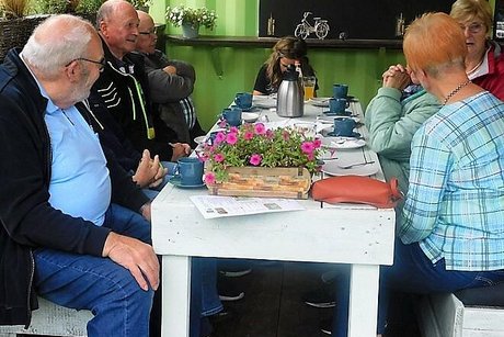 Männer und Frauen sitzen gemeinsam bei Kaffee und Kuchen an einem Tisch.