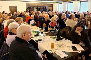 Viele Menschen sitzen an Tischen in einem Saal