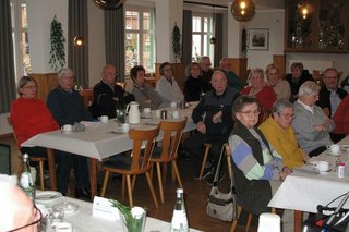 Viele Menschen sitzen in einem Saal an langen Tischen.