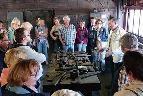 Eine Gruppe Menschen steht um einen Tisch herum, auf dem verschiedene alte Werkzeuge ausgestellt sind, mit denen die Zechenarbeiter damals gearbeitet haben.