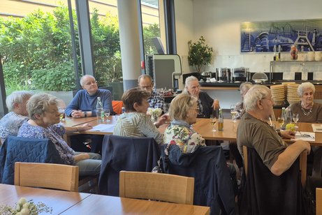 Mitglieder sitzen an Tischen und h&ouml;ren dem Vortrag zu.