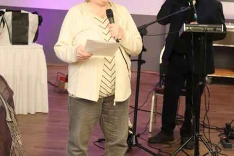 Eine Frau h&auml;lt einen Vortrag , im Hintergrund steht ein Musiker.