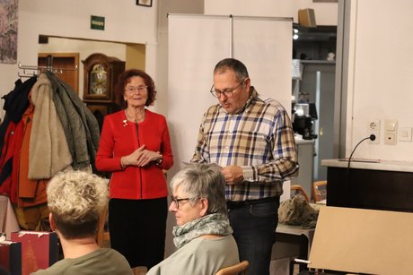 Eine Frau und ein Mann stehen vor den Mitglieder und sprechen zu ihnen.