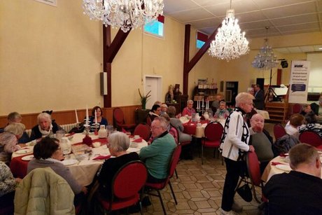 Viele Menschen sitzen an festlich eingedeckten Tischen in einem Saal.