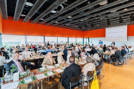 Viele Menschen sitzen an langen festlich gedeckten Tischen.