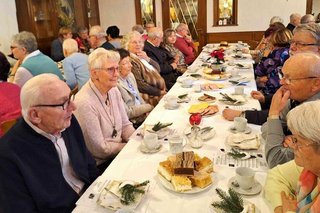 Viele Menschen sitzen an festlich eingedeckten Tischen in einem Saal