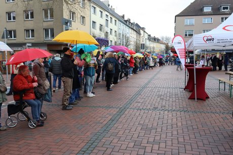 Viele Menschen stehen mit bunten Schirmen nebeneinander.