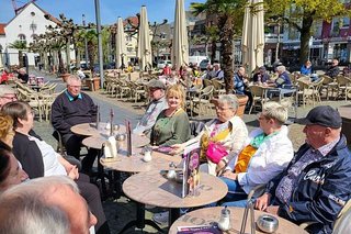 Eiscafé-Pause beim Stadtbummel: Menschen sitzen gemeinsam um Bistrotische herum an einem sonnenbeschienenen Platz in der Xantener Altstadt.