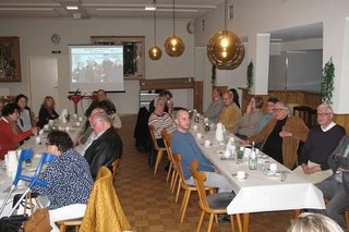 Viele Menschen sitzen in einem Saal an langen Tischen.